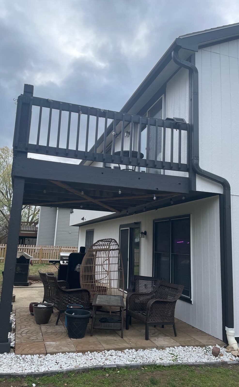 Two-story home exterior with freshly painted white siding and black trim, featuring a black-painted elevated deck and patio seating area underneath.